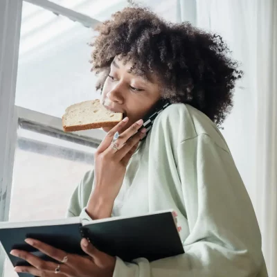 A woman multitasks—talking on the phone while holding a slice of bread in her mouth