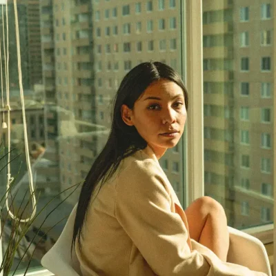 Woman sitting near window in city light.