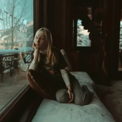 Woman sitting by a window, looking thoughtful.